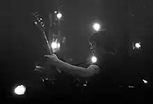 Une photographie en noir et blanc représentant un homme jouant de la guitare devant des projecteurs d'éclairage.