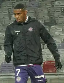 Plan américain d'Ado Onaiwu, short violet, gants et survêtement noir.