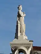 Photo de la statue en pierre calcaire claire d'une jeune femme couronnée appuyée contre une représentation du clocher de la cathédrale Saint-Front.