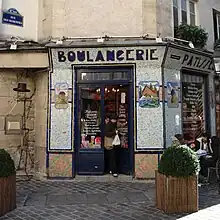 Boulangerie-pâtisserie au coin de la rue des Rosiers avec une devanture en mosaïques.
