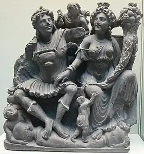Le couple protecteur Panchika et Hārītī (à la corne d'abondance). Takht-i-Bahi, Gandhara. IIe – IIIe&nbsp;siècle. Schiste. British Museum.