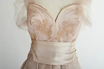 Une robe en satin rose avec une superposition de dentelle appliquée Carrickmacross avec un motif de papillon et de petites perles.