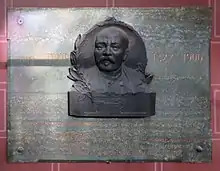 plaque en marbre vert sur laquelle est apposé le portrait en bronze de Lenoir ;&nbsp;en lettres dorées figure l’inscription suivante : Étienne Lenoir (portrait) 1822 - 1900  Inventer du premier moteur à gaz industriel 1860  Plaque commémorative érigée par souscription sur  l'initiative de la Chambre Syndicale de l’Industrie des moteurs  à gaz, à pétrole et des gazogènes le 16 décembre 1912 Monsieur Fernand David, ministre du commerce et de l’Industrie (J. Malet)