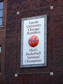 Sur un mur en briques rouges, un panneau blanc avec au centre un ballon marqué 1963, année du titre de l'équipe masculine des Ramblers de Loyola.