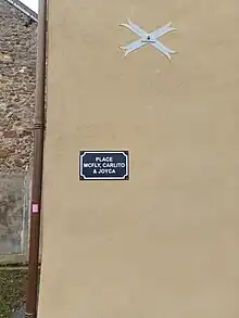 Photographie en couleurs d'une plaque de rue bleue sur un mur beige.