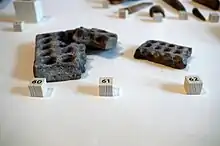 Photographie en couleurs de plaques en terre cuites creusées d'alvéoles alignées.