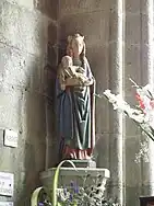 Vue de face, dans un angle, debout. Couronne dorée. Vêtue de bleu et de rose. Entourée de fleurs et d'ex-votos.