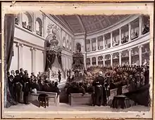 Tableau montrant des hommes assis dans des gradins regardant un homme en uniforme debout