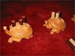 photographie en gros plan de deux tortues sculptées dans du bois. Le dos des tortues est percé de trous ronds dans lesquels sont posés des pions cylindriques de deux couleurs différentes