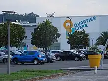 Photographie en couleurs d'un centre commercial et d'un parking.