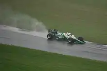 Photo d'une monoplace verte et blanche sur une piste détrempée