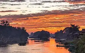 Nuages rouges au-dessus des berges du Mékong avec des habitations et des pirogues au lever du soleil à Don Det. Janvier 2024.