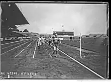 Photographie en noir et blanc d'un homme en tenue de sport, franchissant une ligne d'arrivée. Il s'agit de René Wiriath. Il porte le dossard no&nbsp;90. En arrière-plan, un groupe de 3 coureurs se présente sur la ligne d'arrivée.