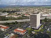 Panorama d'Oxnard en 2012. Au premier plan, un grand parking, quelques bâtiments et le siège de la City National Bank d'Oxnard, qui domine la ville. Au second plan, le reste de la ville. En arrière-plan, des prés, u bois et des montagnes.