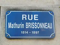 Plaque rectangulaire indiquant «&nbsp;rue Mathurin Brissonneau 1814-1897&nbsp;» en blanc sur fond bleu.