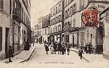 Carte postale sépia d'une rue au début des années 1900. Des enfants prennent la pose au milieu de la voie. Légende : « Saint-Denis, rue du Saulger ».