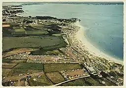 Photo aérienne montrant le littoral d'une plage. Les champs attenants sont remplis de tentes de camping.