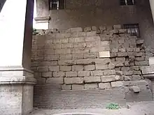 Photographie en couleurs d'un mur en moellons réguliers sous une arche maçonnée.