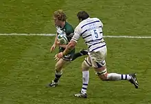 Photo de Sam Vesty courant avec le ballon tout en essayant d’éviter le placage de Peter Short.