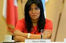 Femme d'une quarantaine d'années, à la peau mate et aux cheveux noirs, croisant les bras sur une table où reposent une tasse à café, un verre d'eau et un petit carton indiquant "Samia Ghali".