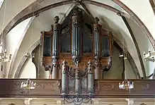 photographie en couleur montrant un orgue dont le buffet en bois foncé est monté sur une tribune et touche presque la voûte au dessus de lui