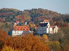 Vue d'un grand bâtiment à la façade blanche et au toit rouge au milieu d'une forêt.