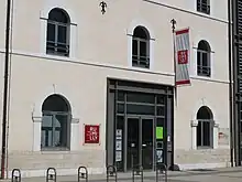 Photographie en couleurs et de légèrement en biais de la façade d'un bâtiment gris et beige