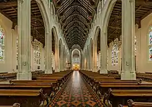 Une grande allée centrale dans un long batiment vouté bordé de piliers et rempli de bancs bien alignés.