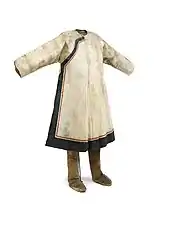 Manteau en peau de saumon de coupe chinoise avec fermeture asymétrique et passementerie en peau de poisson noire et rouge. Bottes en peau de renne, côté poil vers l'intérieur. Le côté chair est teint en brun, et la bordure est en tissu brun, rouge et noir. Peuple nivkh.