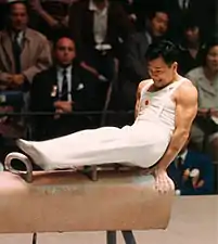 Un homme en tenue blanche avec ses deux mains sur un cheval d'arçon.
