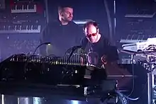 photo de deux hommes entourés de synthétiseurs.