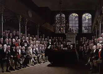 William Pitt le jeune s'adressant à la chambre des communes répartie de chaque coté de la pièce sur des tribunes.
