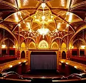 Photographe d'une grande salle comportant une scène avec un rideau foncé, des boiseries et un chandelier au plafond.