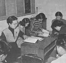 Agenouillés autour d'une table basse, une réalisatrice, ses acteurs et ses actrices font la lecture du script d'un film (image en noir et blanc).