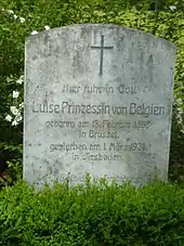 Une petite stèle en pierre claire au sommet arrondi est placé derrière un massif de verdure.