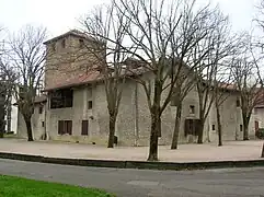Vieille église en pierre avec une tour surélevée. À l'avant, on voit une route et des arbres.