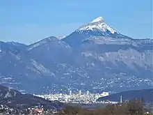 Sommet enneigé dominant des montagnes plus basses et une agglomération.