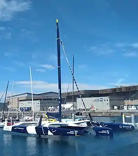 Trimaran bleu et blanc vu de trois quarts avant, amarré au ponton.