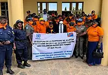 Photographie couleur d'un groupe de femmes portant des t-shirts oranges et tenant une affiche "contre les violences faites aux femmes et aux filles".
