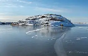 L'île de Vassholmen en sortant du port de Väjern, à Kungshamm. À l'intérieur de cette baie abritée, la glace s'est formée pendant les jours calmes, la rendant claire et "noire". Le panneau de signalisation est l'un des nombreux qui se trouvent le long de la côte suédoise. Les petites "croix" sont d'anciens dispositifs d'amarrage (une sorte de bollards ou de taquets) du début du 20e siècle. Février 2021.
