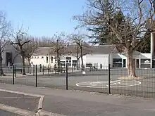 Photographie en couleurs d'une cours avec des dessins au sol ; long bâtiment largement vitré en arrière-plan.