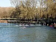 Photographie en couleurs d'un cours d'eau avec des kayaks dans les remous d'un déversoir.