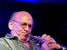 photo d'un homme chauve à lunettes en trian de jouer du saxophone