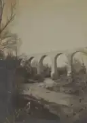 Photographie en sépia d'un cours d'eau serpentant et passant sous l'arche du pont.