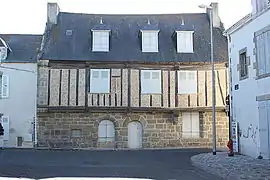 Vue d'une façade de maison en granit, pans de bois et toit d’ardoise.